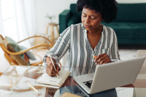 Woman sitting at table and taking notes at home office. African woman working from home.
