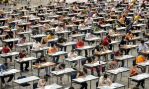 students at rows of desks in an open gym