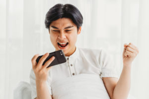 Asian man sitting in bed playing game. The Asian man is getting excited by the victory while playing the mobile game