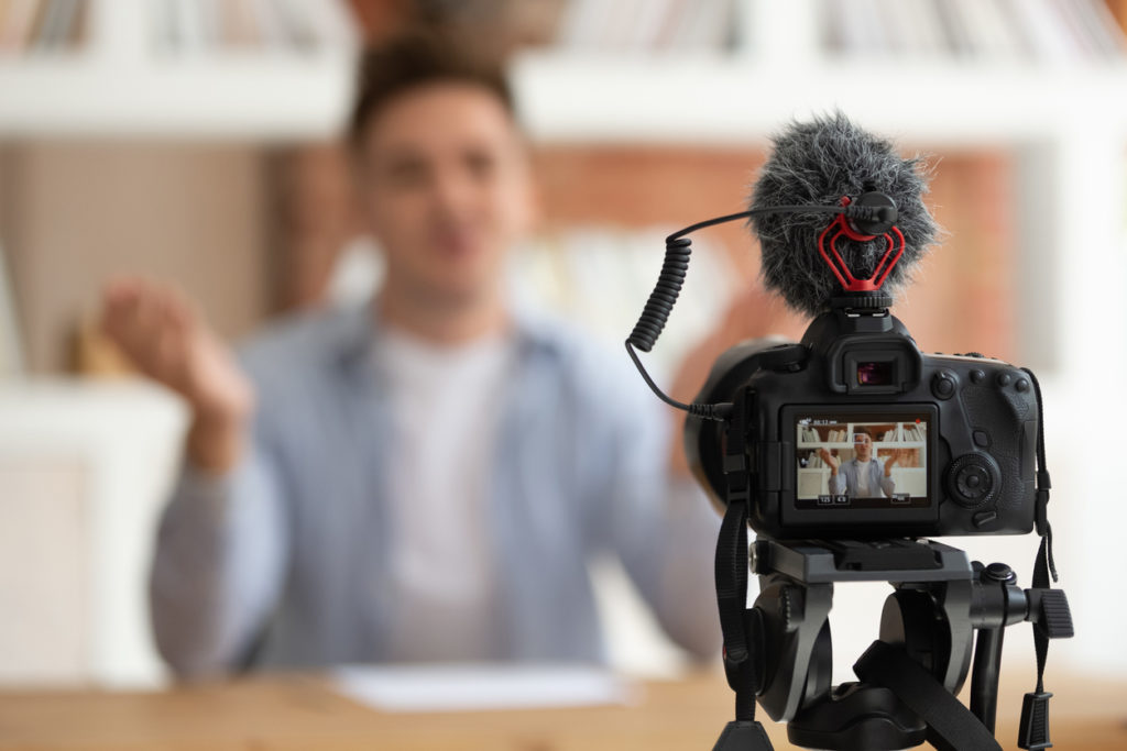 Close up professional digital equipment recording video blog of student shown on screen man sit at desk in front of camera filming online training webinar educational seminar or job interview concept