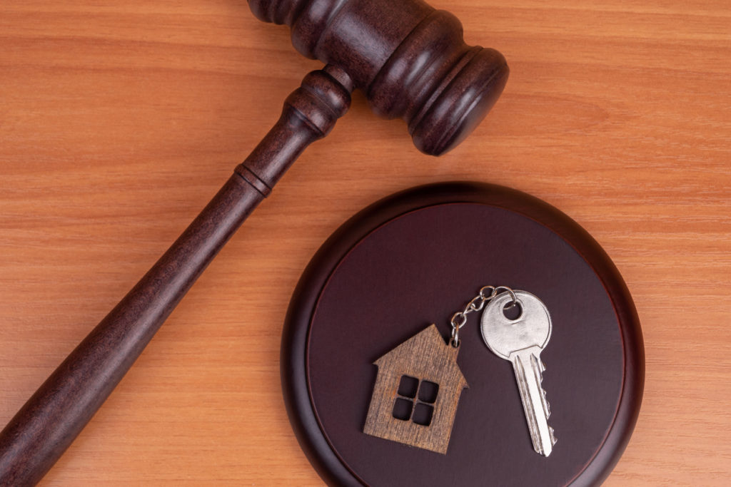 Judge gavel and key chain in shape of two splitted part of house on wooden background