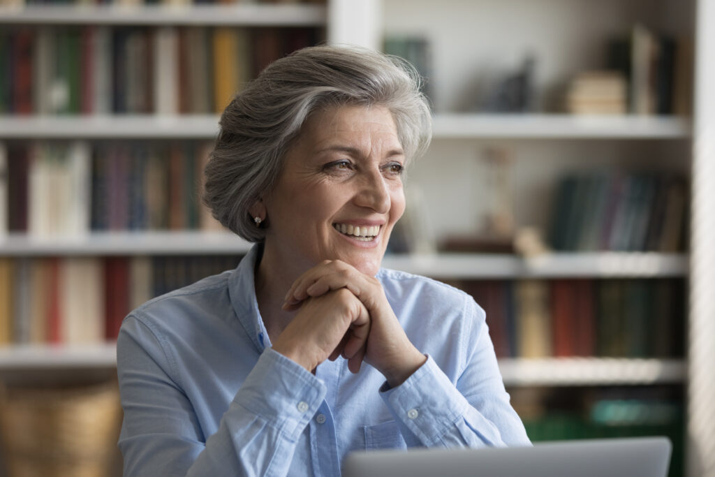 60s businesswoman sit at workplace with laptop distracted from work smile looks aside feel happy, satisfied with workflow, career growth, business success, middle-aged businesslady portrait concept, small law firm lawyer