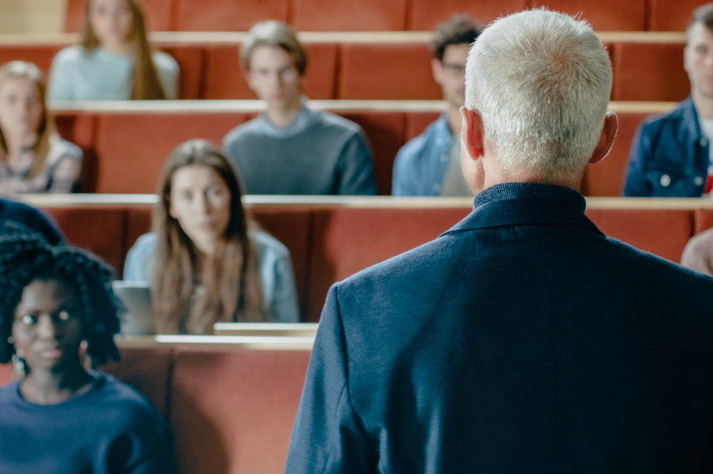 Camera Facing Class: College Professor Gives a Lecture to a Classroom Full of Multi Ethnic Students. Talented Speaker Captures Audience Attention.