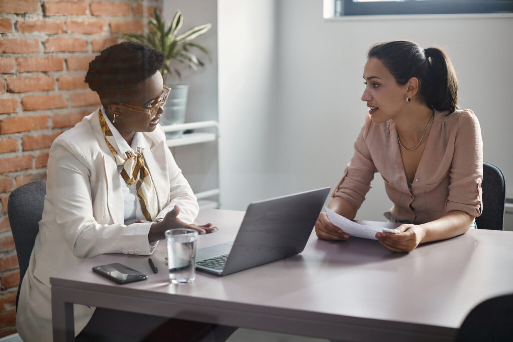 Young woman communicating with African American human resource manager while applying for job at corporate office.