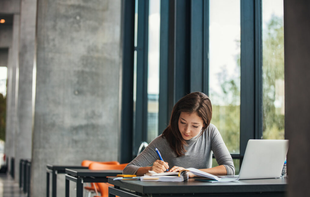 JD-Next Shot of young asian female student sitting at table and writing on notebook. Young female student studying in library.