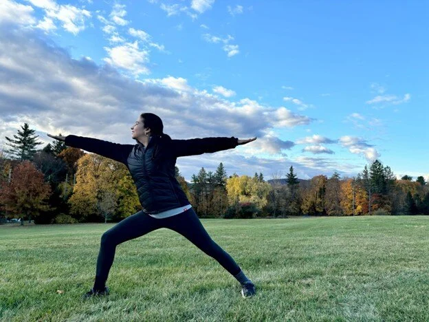 Woman doing a yoga pose in a field with a blue sky