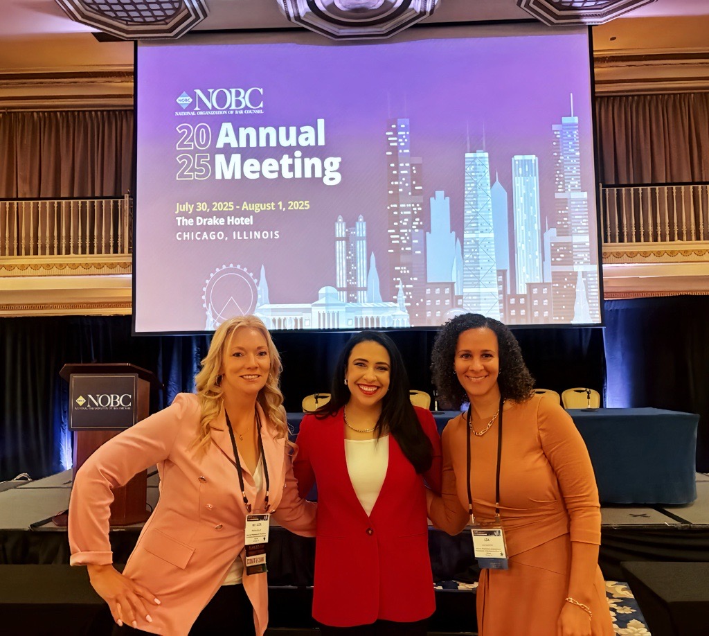 Three women posing in front of a podium and a slide that says the National Organization of Bar Counsel Annual Meeting.