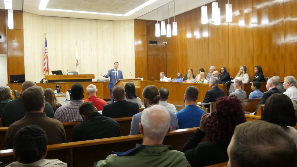 Man standing in a courtroom addressing a large crowd